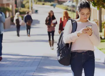 female student walking on campus looking at her phone