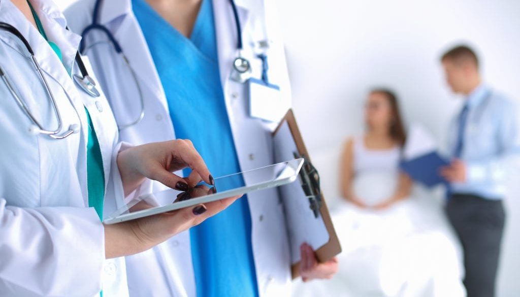 doctor and nurse talking holding tablet with patients in background