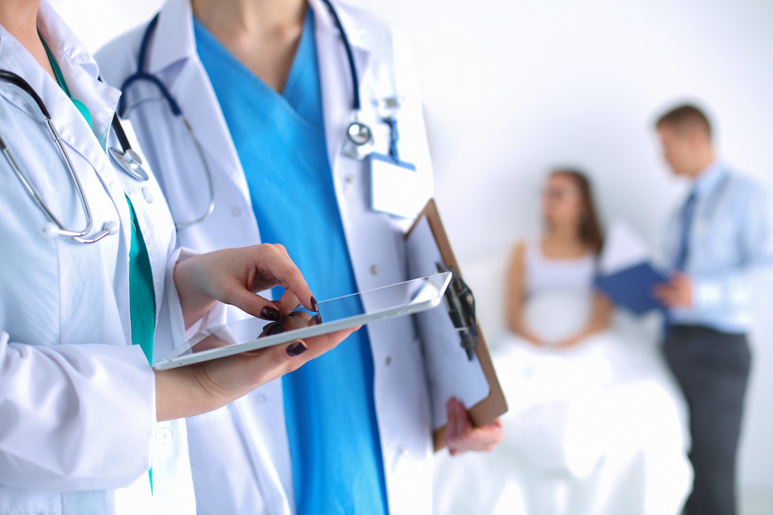 Doctors-nurse-holding-tablet doctor and nurse talking holding tablet with patients in background