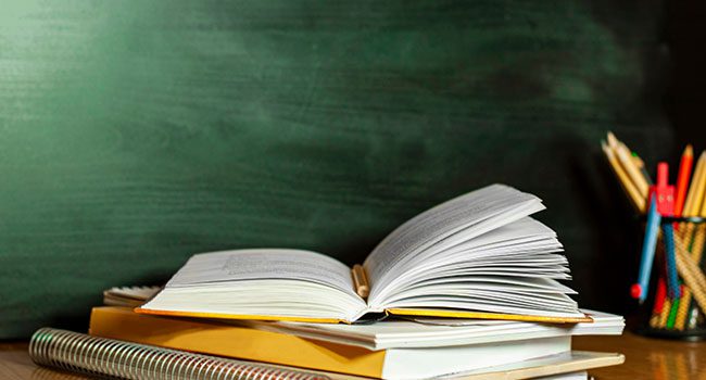 school-books-stacked open text book on desk in front of blackboard