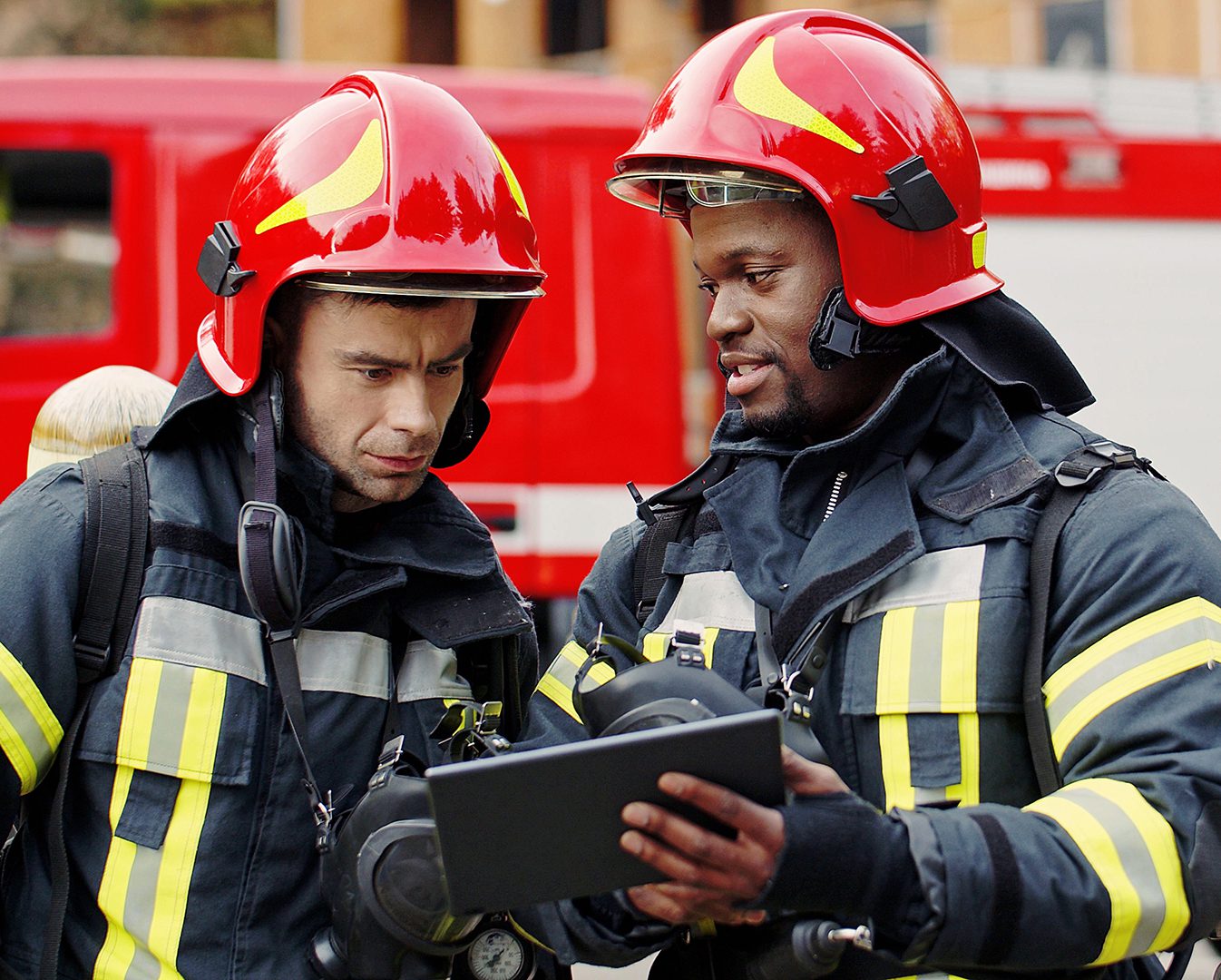 Portrait,Of,Two,Firefighters,In,Fire,Fighting,Operation,,Fireman,In firefighters looking at tablet in uniform at scene of incident