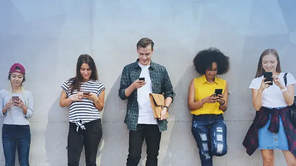 students standing against wall holding cell phones