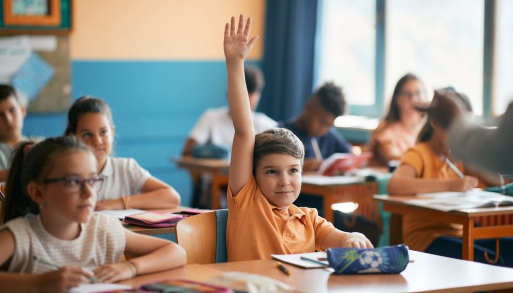 student in classroom smiling raising hand
