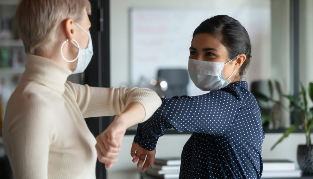 Smiling diverse Female Colleagues Wearing Protective Face Masks Greeting