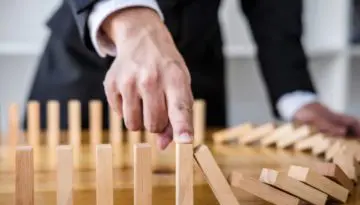 man stopping the domino effect of falling wooden piecees