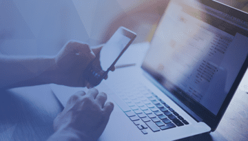 hand holding phone while working on a laptop