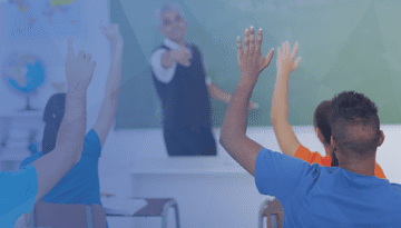 students in classroom with teacher standing at front of class as kids raise hands