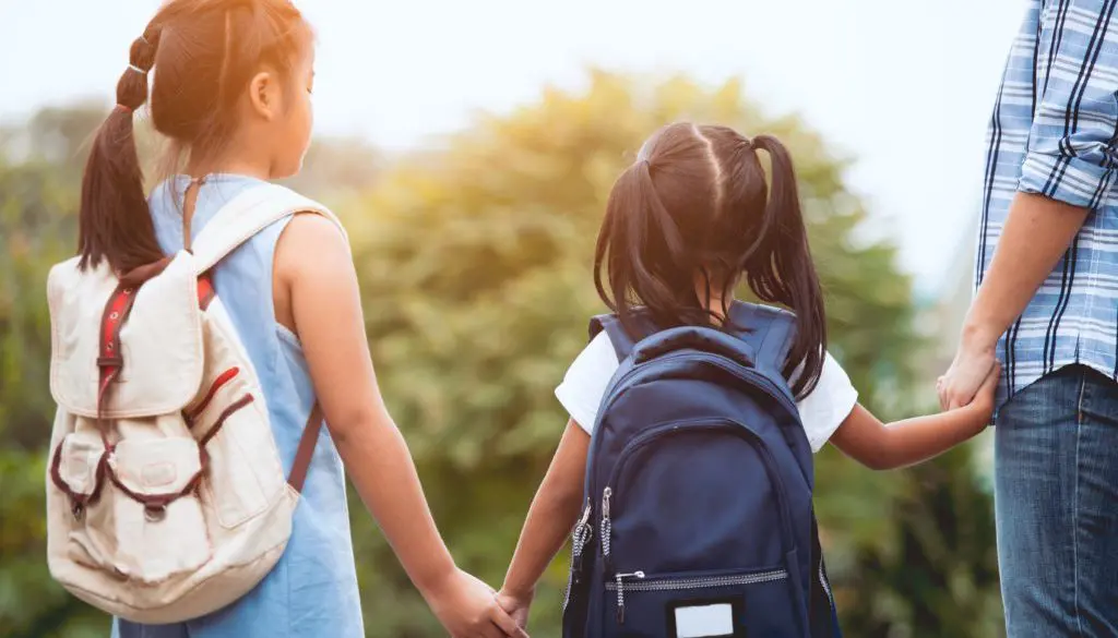 children holding hands with backpacks on