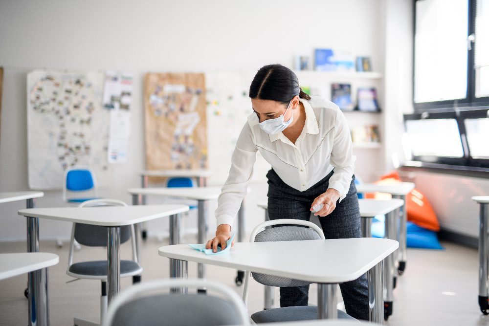 teacher wearing mask in a classroom disinfecting desks