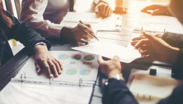 business people gathered around a table, comparing notes