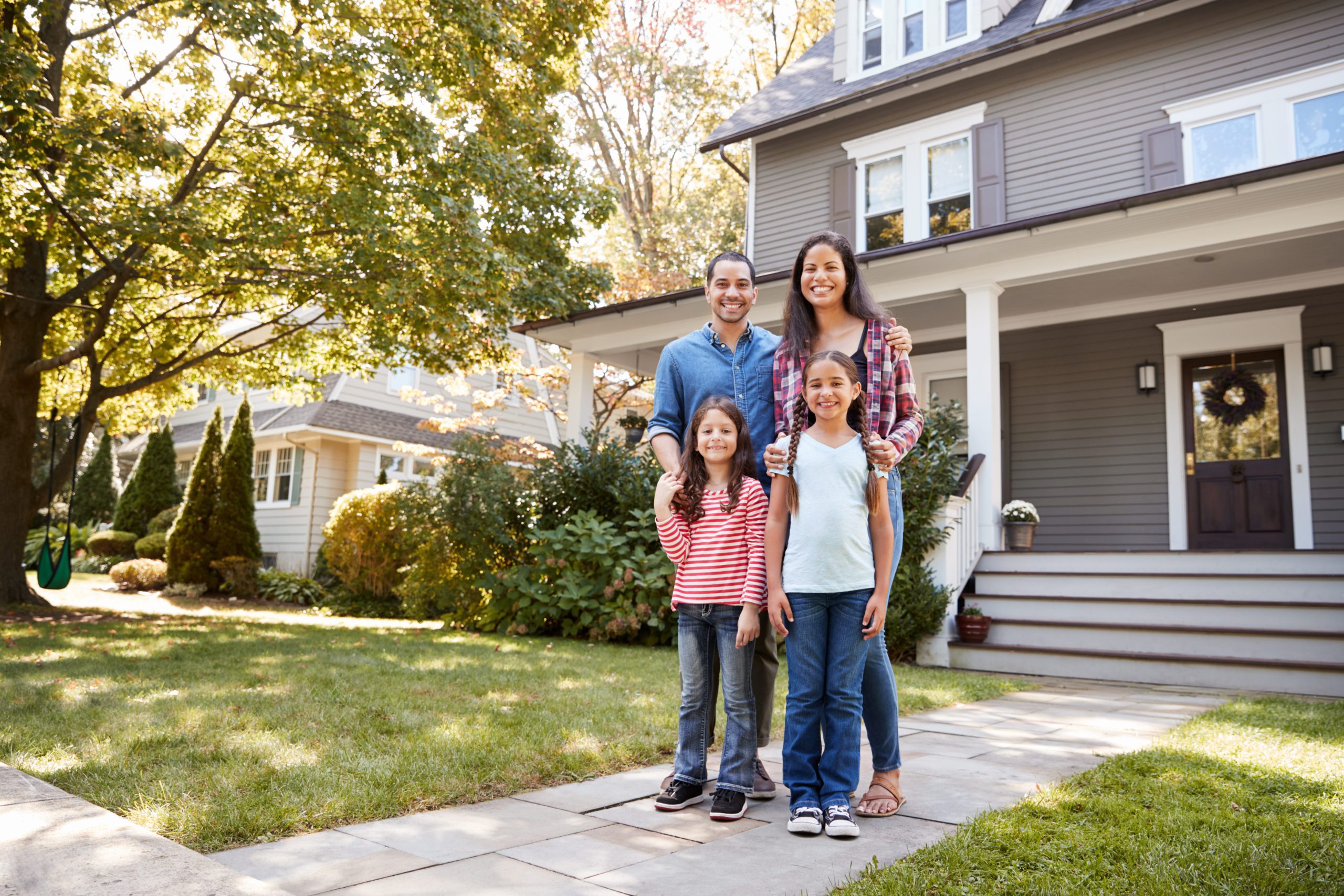 family of four standing in front of their house smiling