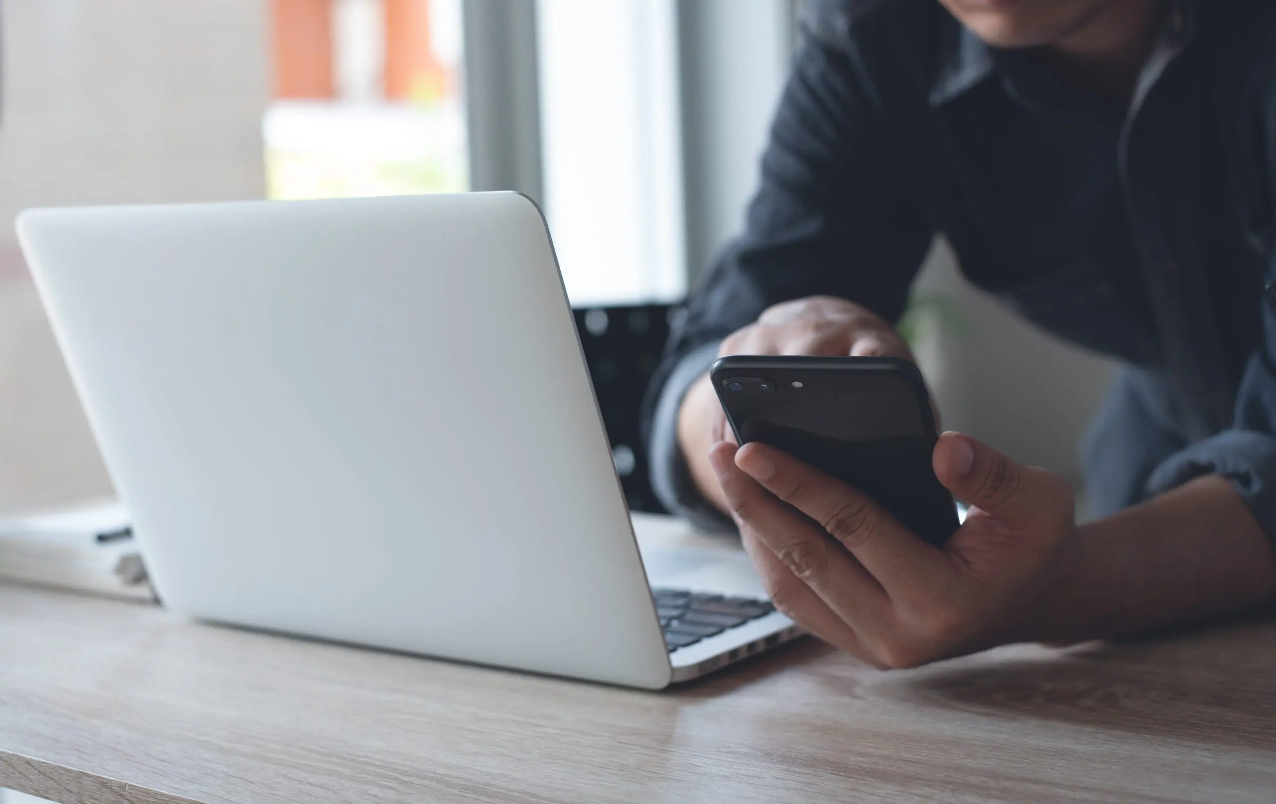 man sitting at desk holding phone with laptop computer on top of his desk