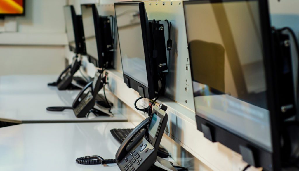 desk in emergency call center with a row of phones and computers