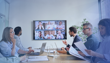 employees working at a conference table with remote employees on tv screen